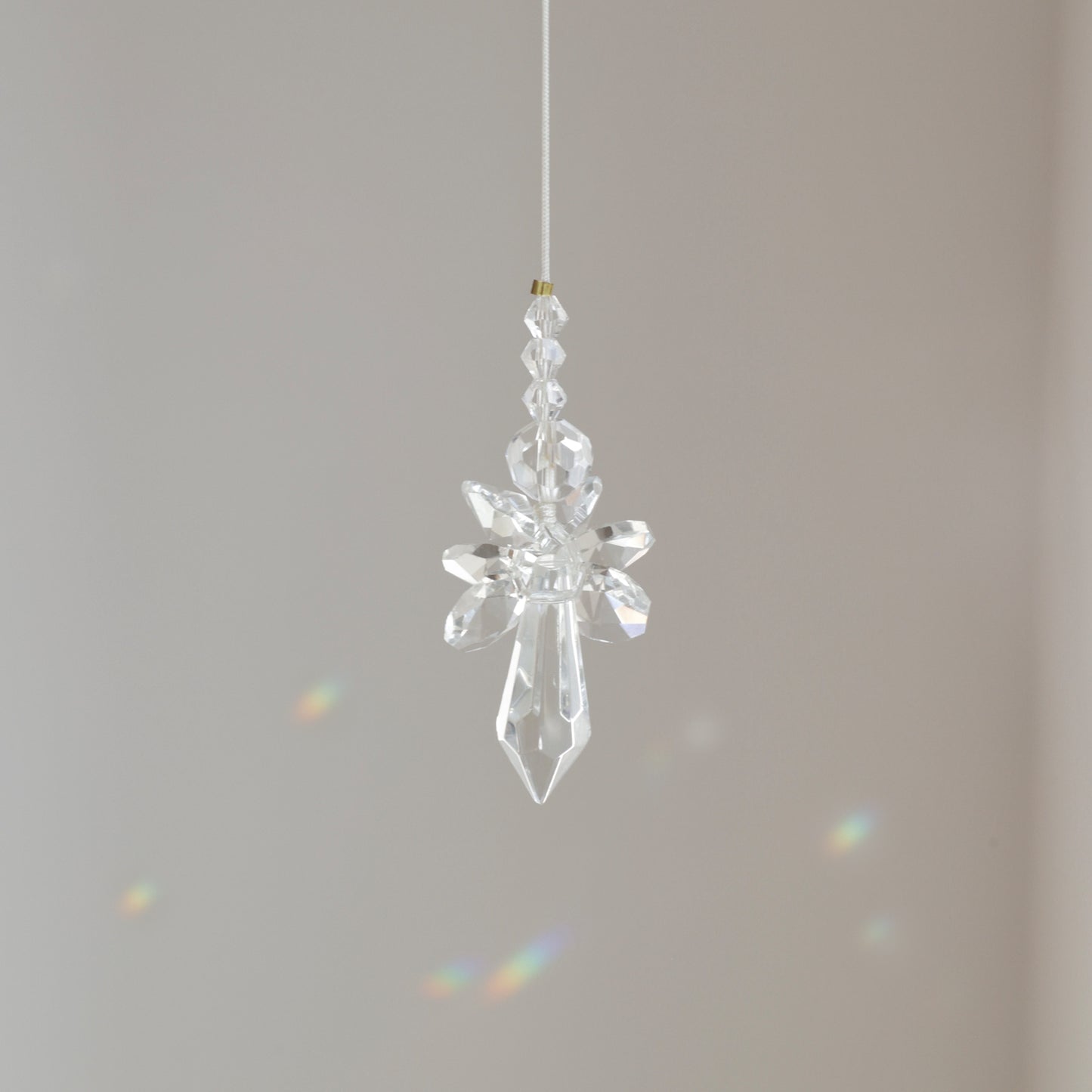 Suncatcher Ange, symbole de protection et de pureté, suspendu à une fenêtre ensoleillée et diffusant des reflets arc-en-ciel.