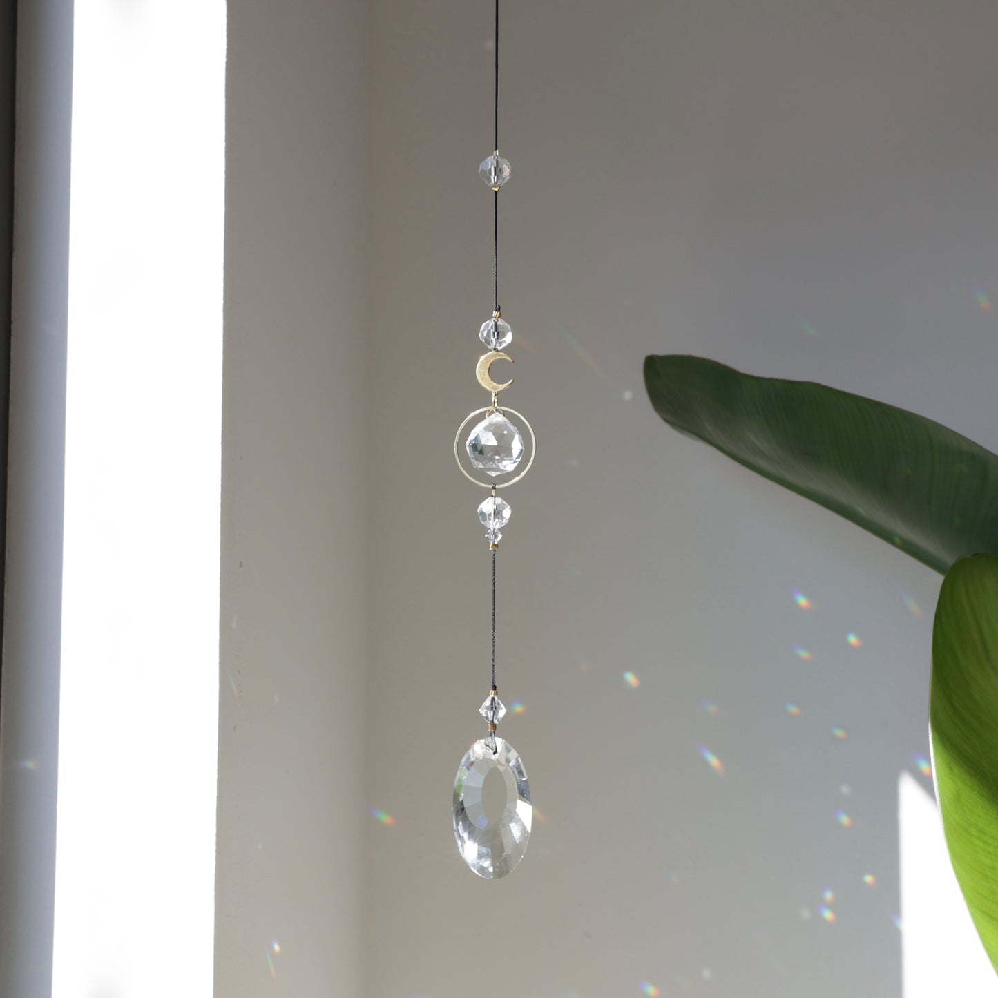 Suncatcher Black Aura suspendu près d’une fenêtre, reflétant la lumière du soleil en éclats colorés.