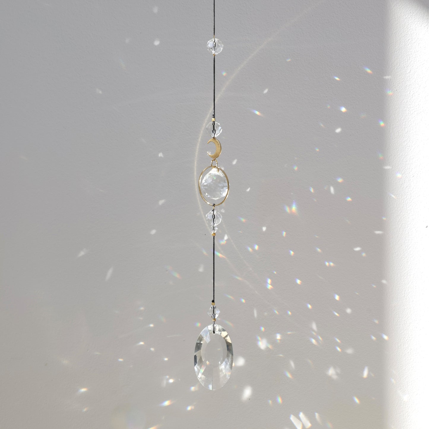 Attrape-lumière Rayonne® suspendu devant une fenêtre ensoleillée, diffusant des reflets magiques dans la pièce.