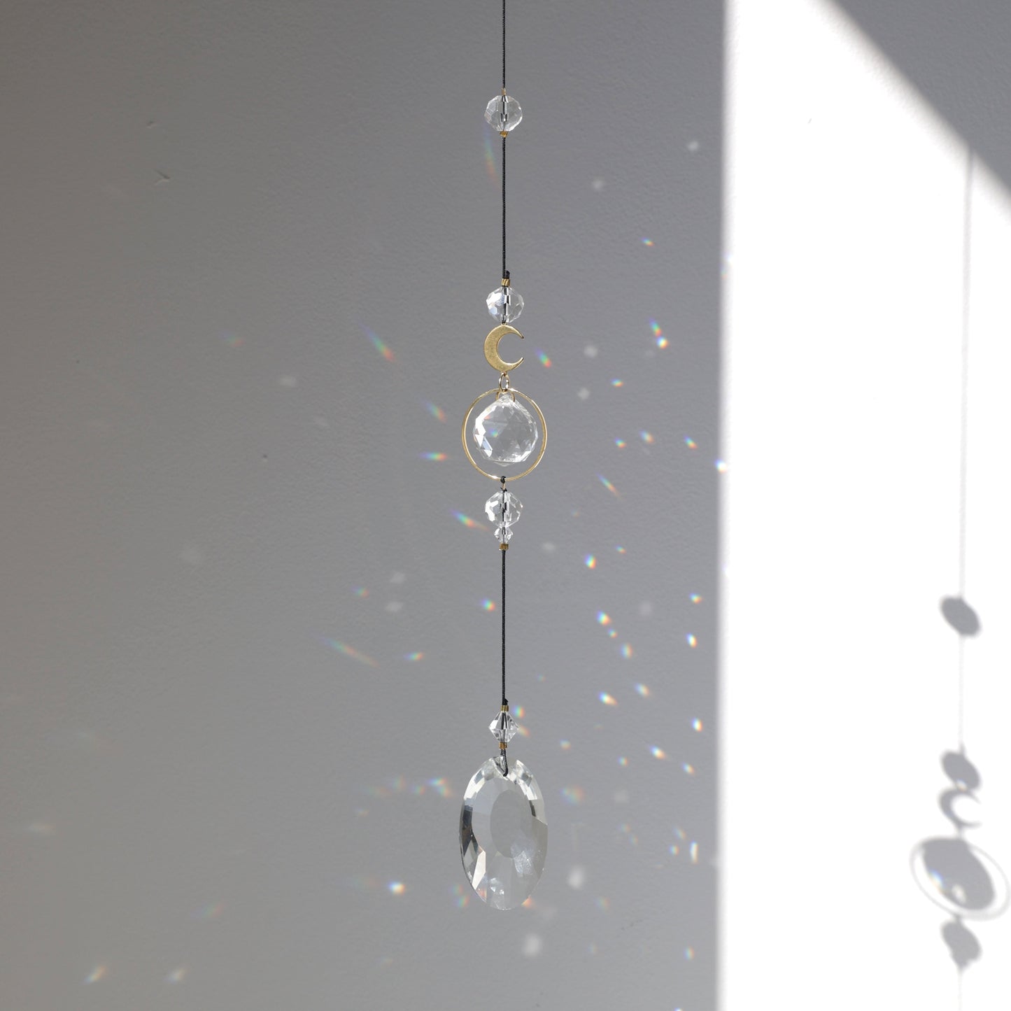 Suncatcher Black Aura de la marque Rayonne suspendu à une fenêtre, capteur de lumière créant des arcs-en-ciel dans la maison.