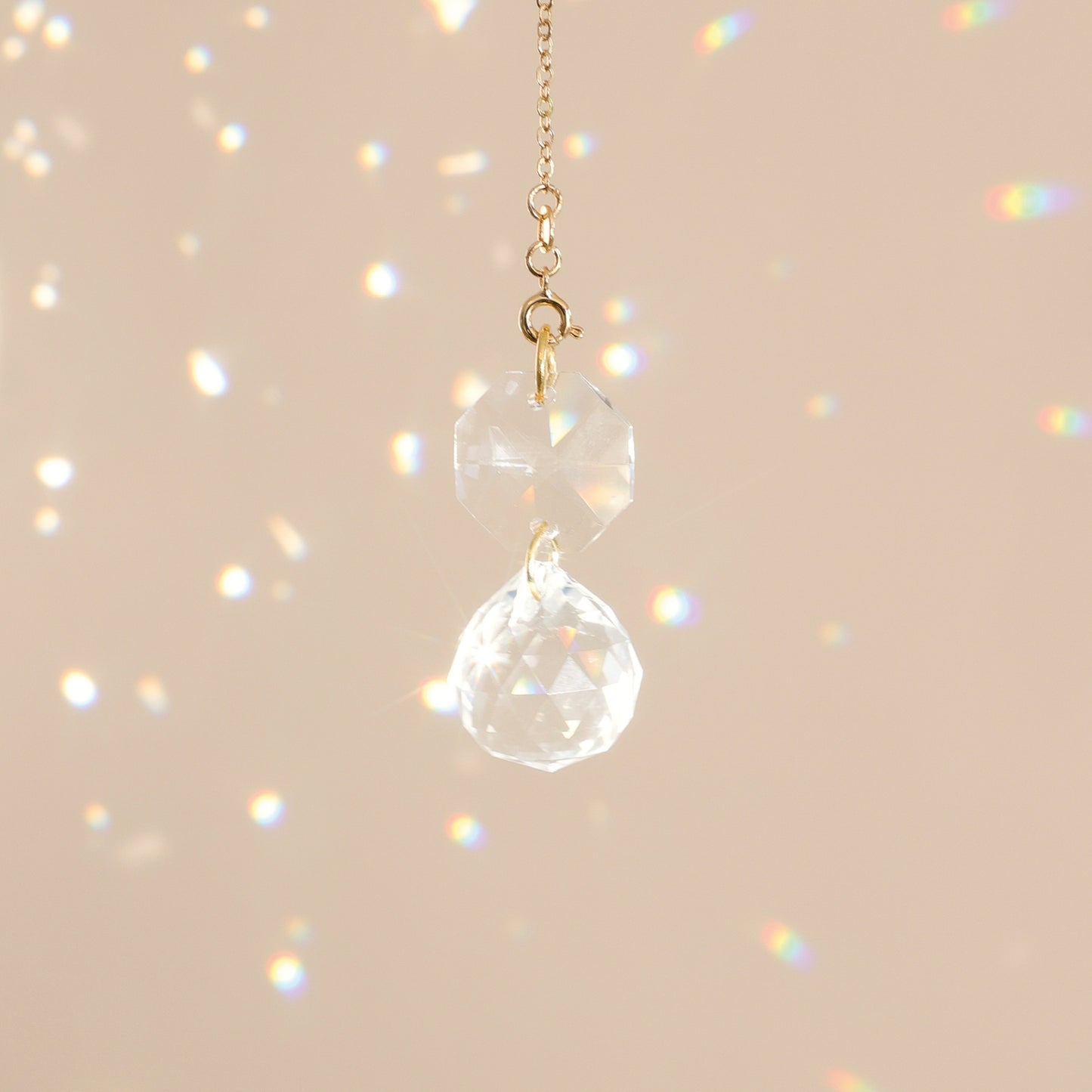 Mini Suncatcher CARAT suspendu près d’une fenêtre, diffusant des reflets arc-en-ciel et créant une ambiance harmonieuse et apaisante.