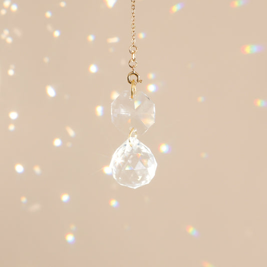Mini Suncatcher CARAT suspendu près d’une fenêtre, diffusant des reflets arc-en-ciel et créant une ambiance harmonieuse et apaisante.