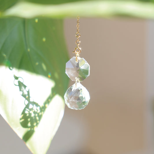 Mini Suncatcher CARAT accroché à une plante, diffusant des reflets arc-en-ciel et apportant énergie positive et douceur.