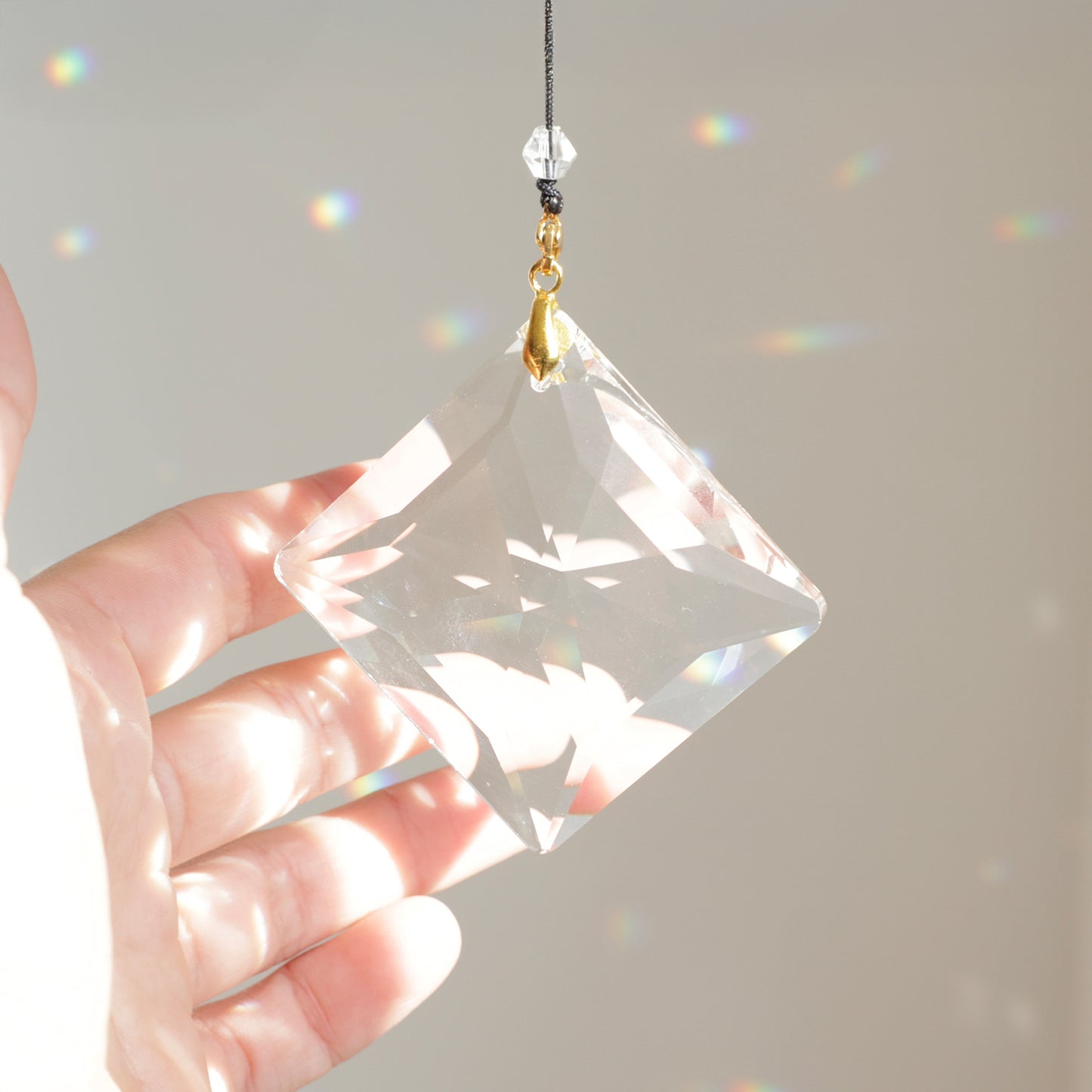 Suncatcher ZENITH, cristal de 7 cm, suspendu à une fenêtre et diffusant des reflets arc-en-ciel lumineux.