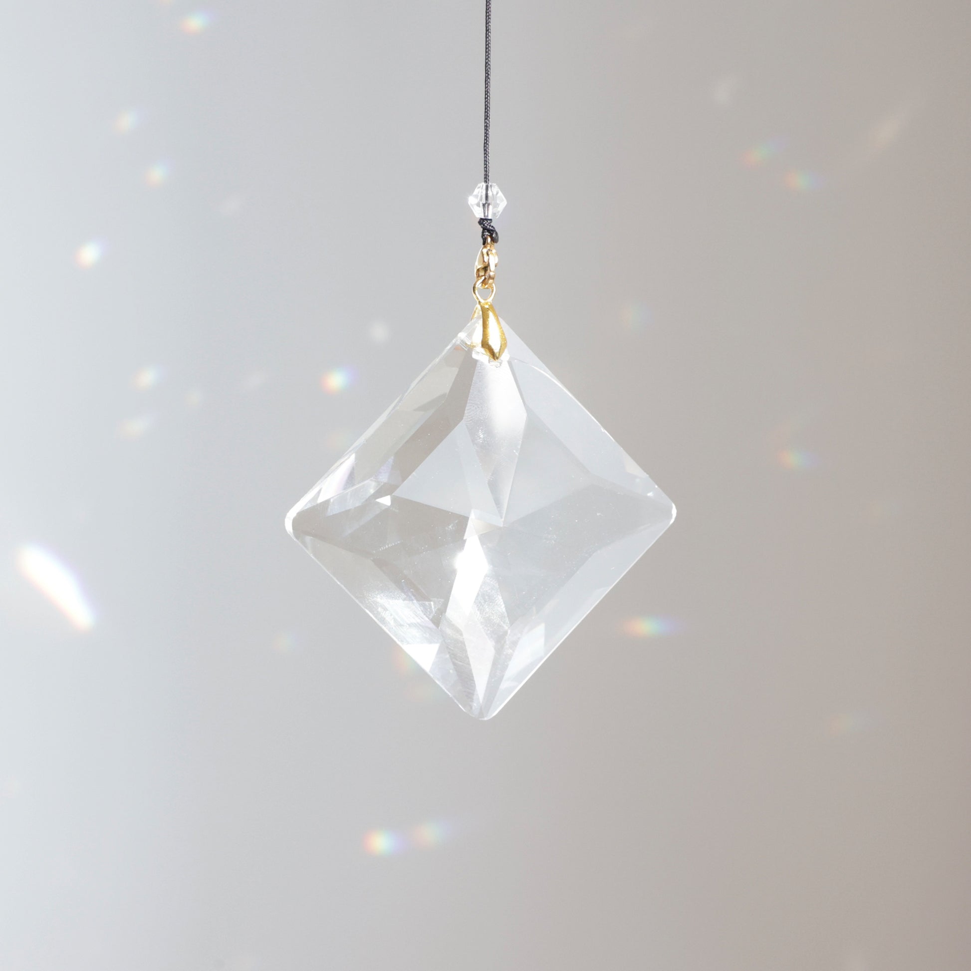 Suncatcher ZENITH clipé sur une rallonge, suspendu au soleil, diffusant des reflets colorés et illuminant la pièce.