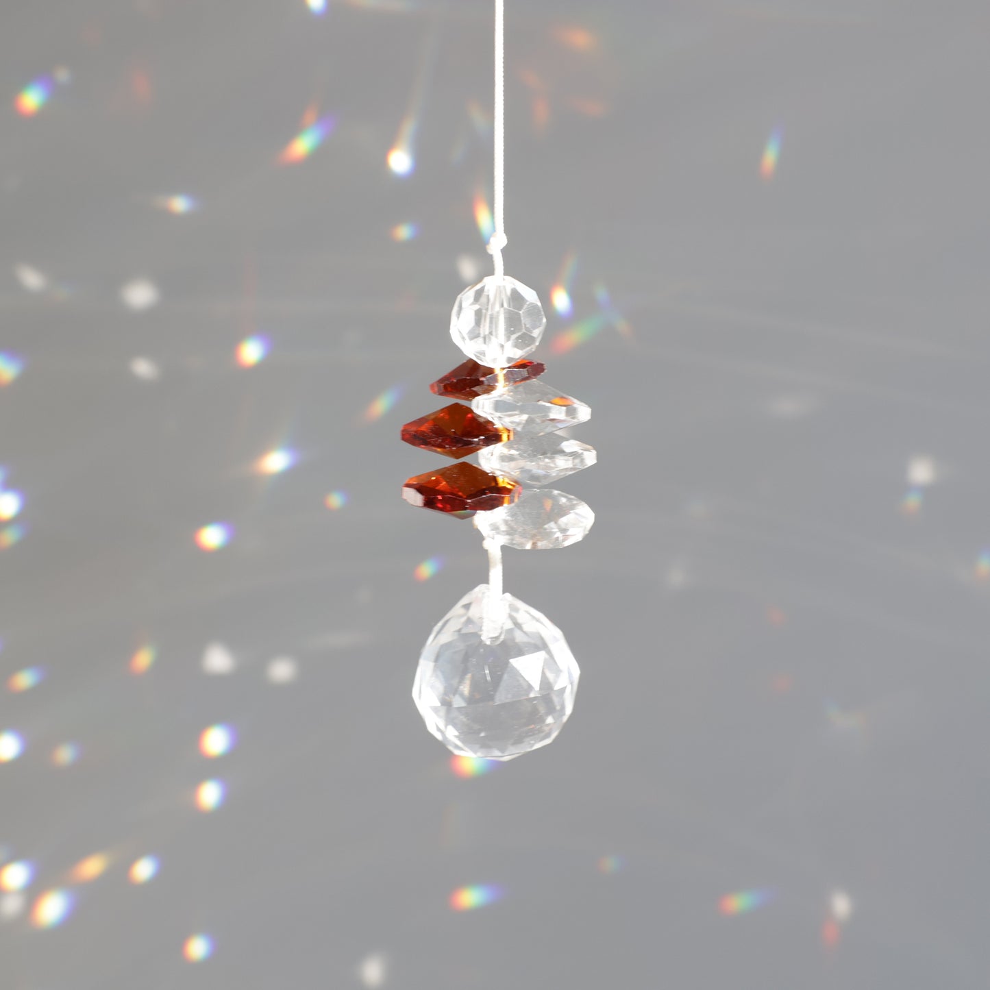 Suncatcher accroché au soleil grâce à sa corde en coton, diffusant des refelts arcs-en-ciel dans la pièce