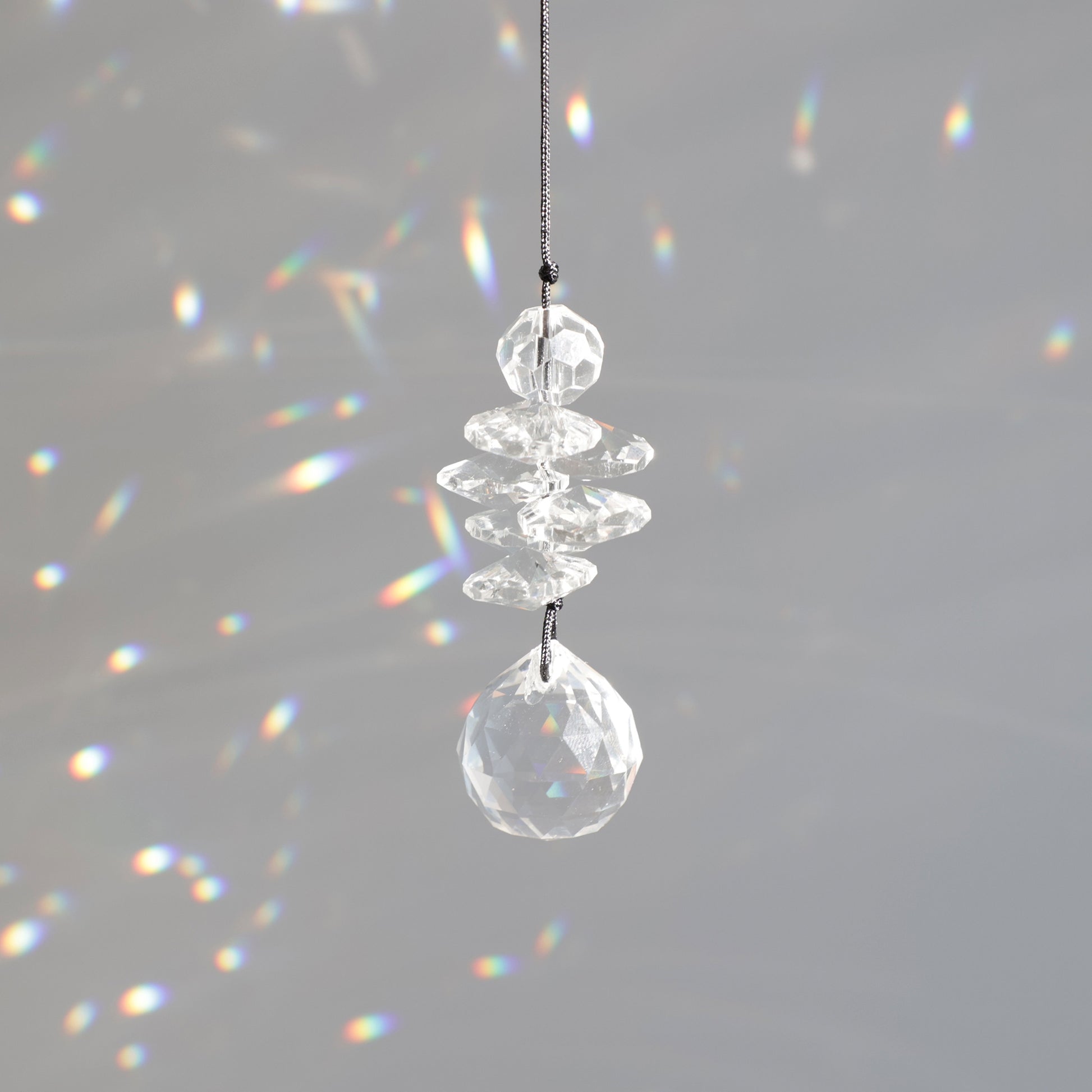 Mini Suncatcher Black Aura de la marque Rayonne® suspendu près d’une fenêtre, reflétant des couleurs arc-en-ciel dans une pièce lumineuse.