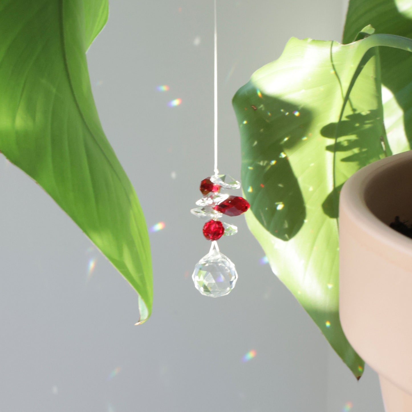 Attrape soleil rouge et transparent, symbole de vitalité, créant des reflets arcs en ciel quand il est placé au soleil