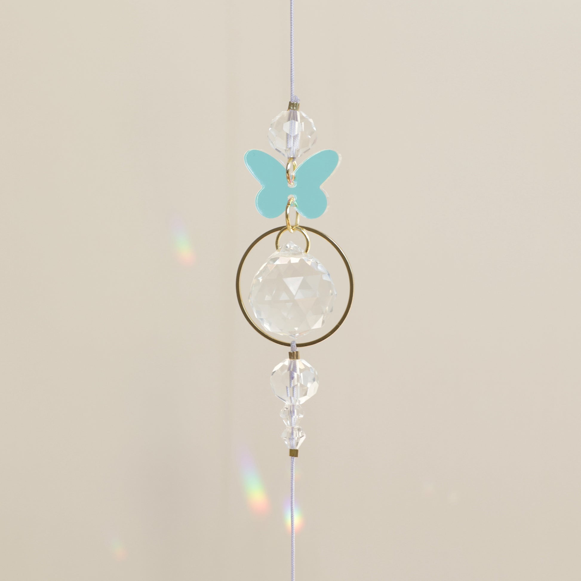 Gros plan sur le charm papillon en acrylique holographique de la rallonge LUEUR, symbole de transformation et de renouveau.