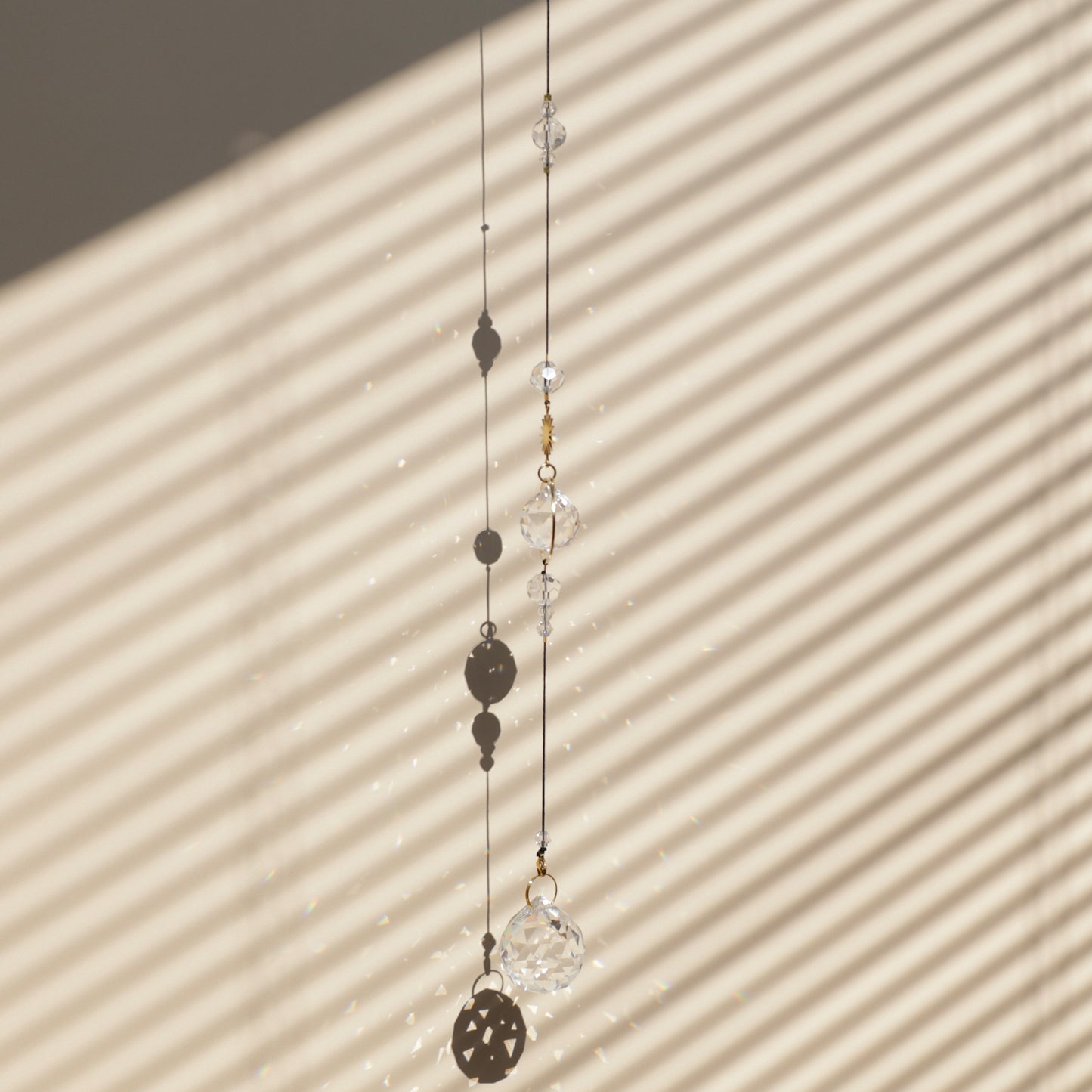 Rallonge HOPE de la marque Rayonne® clipée à un Suncatcher, suspendue près d’une fenêtre ensoleillée, projetant de magnifiques reflets arc-en-ciel dans la pièce.