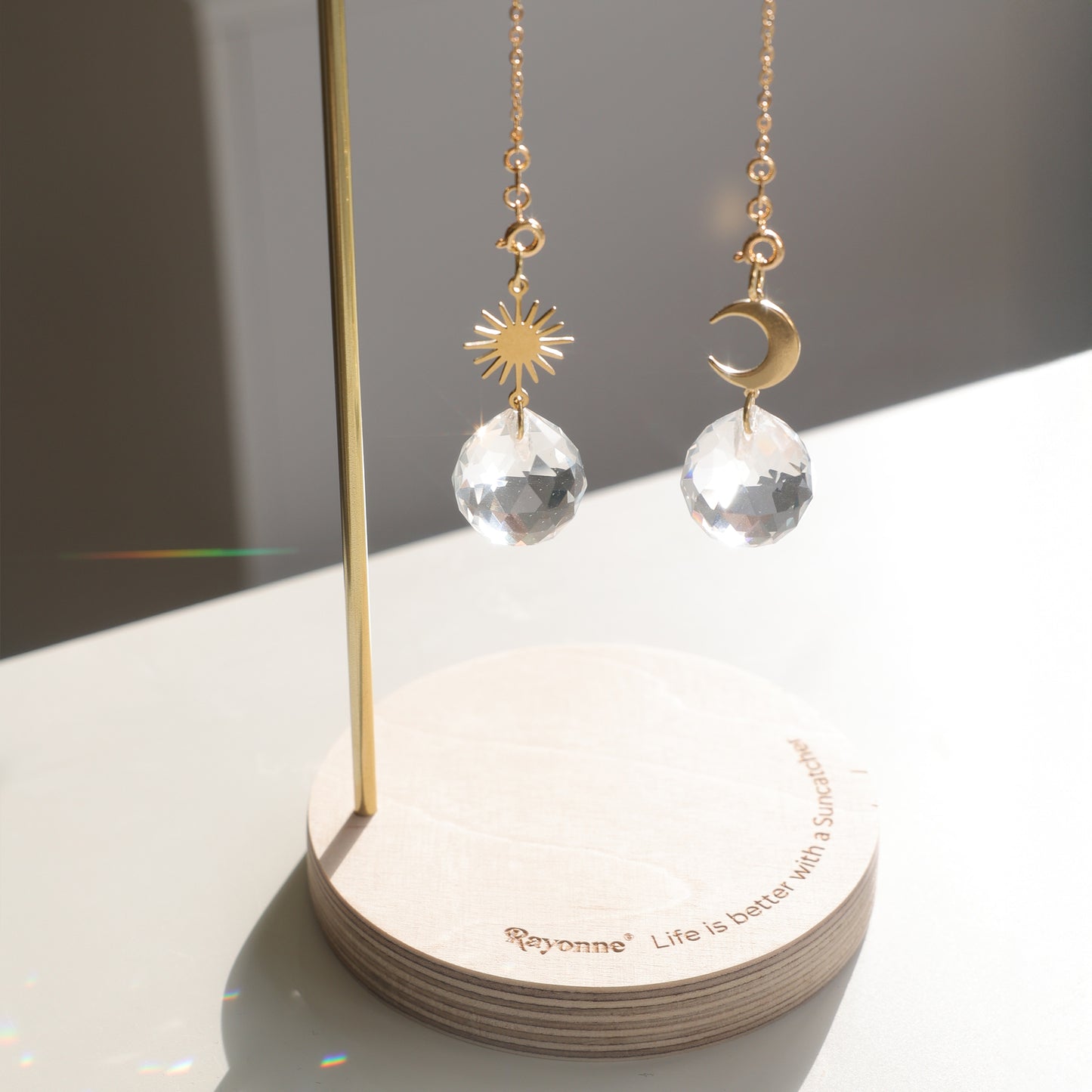 Détail des Suncatchers Rayonne installés sur le présentoir, captant la lumière et créant des reflets arc-en-ciel.