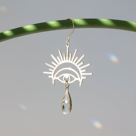 Suncatcher de plante avec un oeil doré, accroché à une tige et diffusant des reflets arcs-en-ciel dans la pièce