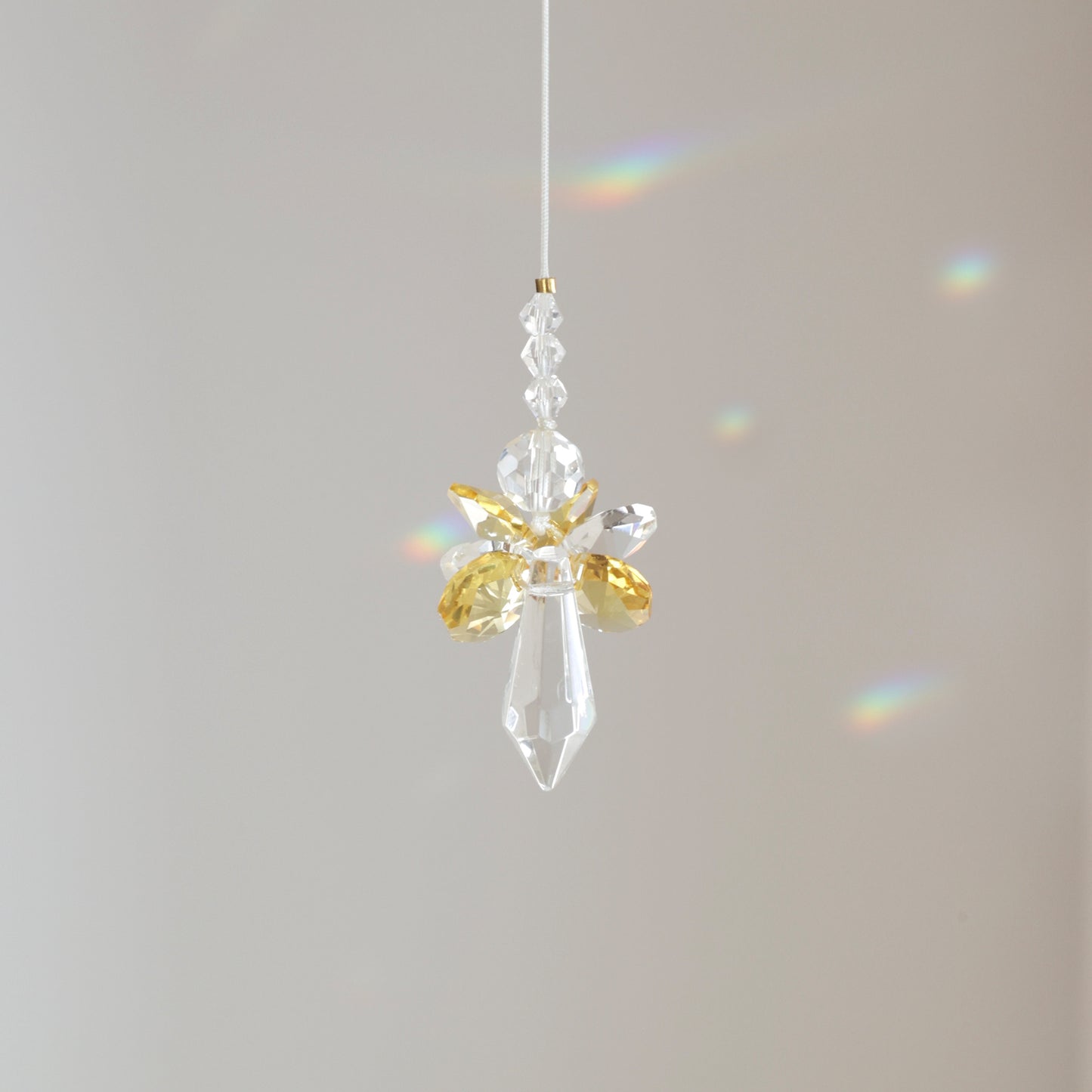 Suncatcher ANGE, symbole de joie et d’énergie, suspendu à une fenêtre ensoleillée et diffusant des reflets arc-en-ciel. Cadeau de naissance