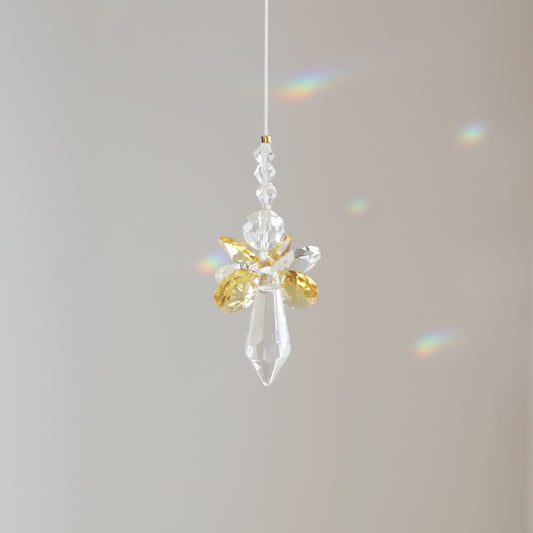 Suncatcher ANGE, symbole de joie et d’énergie, suspendu à une fenêtre ensoleillée et diffusant des reflets arc-en-ciel. Cadeau de naissance