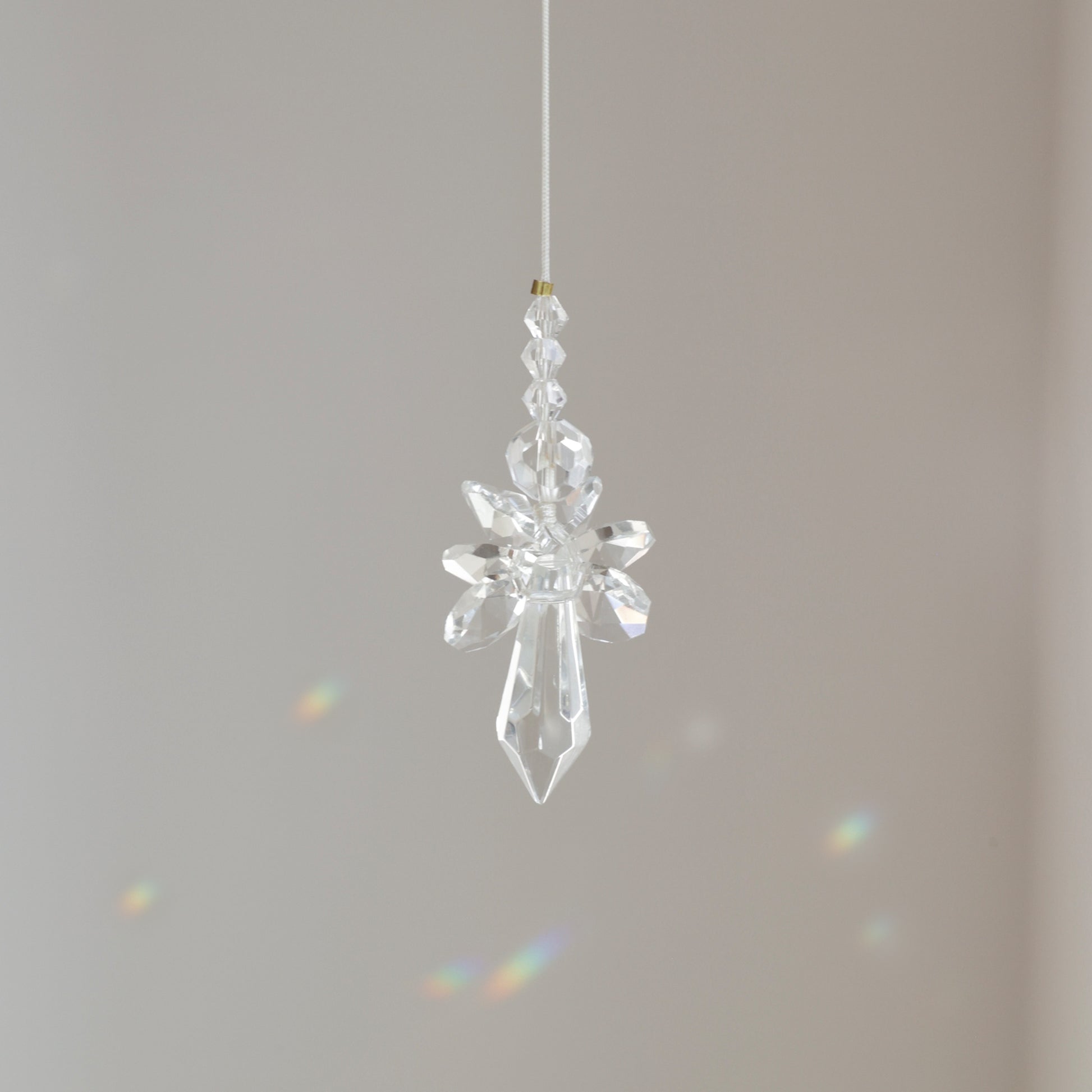 Suncatcher Ange, symbole de protection et de pureté, suspendu à une fenêtre ensoleillée et diffusant des reflets arc-en-ciel.