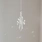 Suncatcher Ange, symbole de protection et de pureté, suspendu à une fenêtre ensoleillée et diffusant des reflets arc-en-ciel.