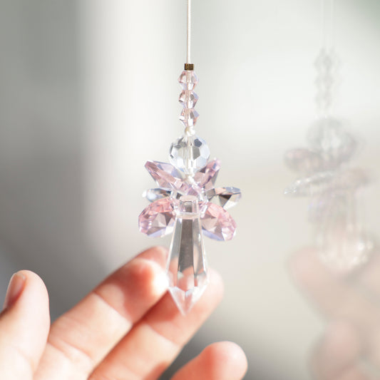 Suncatcher ANGE ce couleur rose  accroché près d’une fenêtre, grâce à la ventouse fournie.