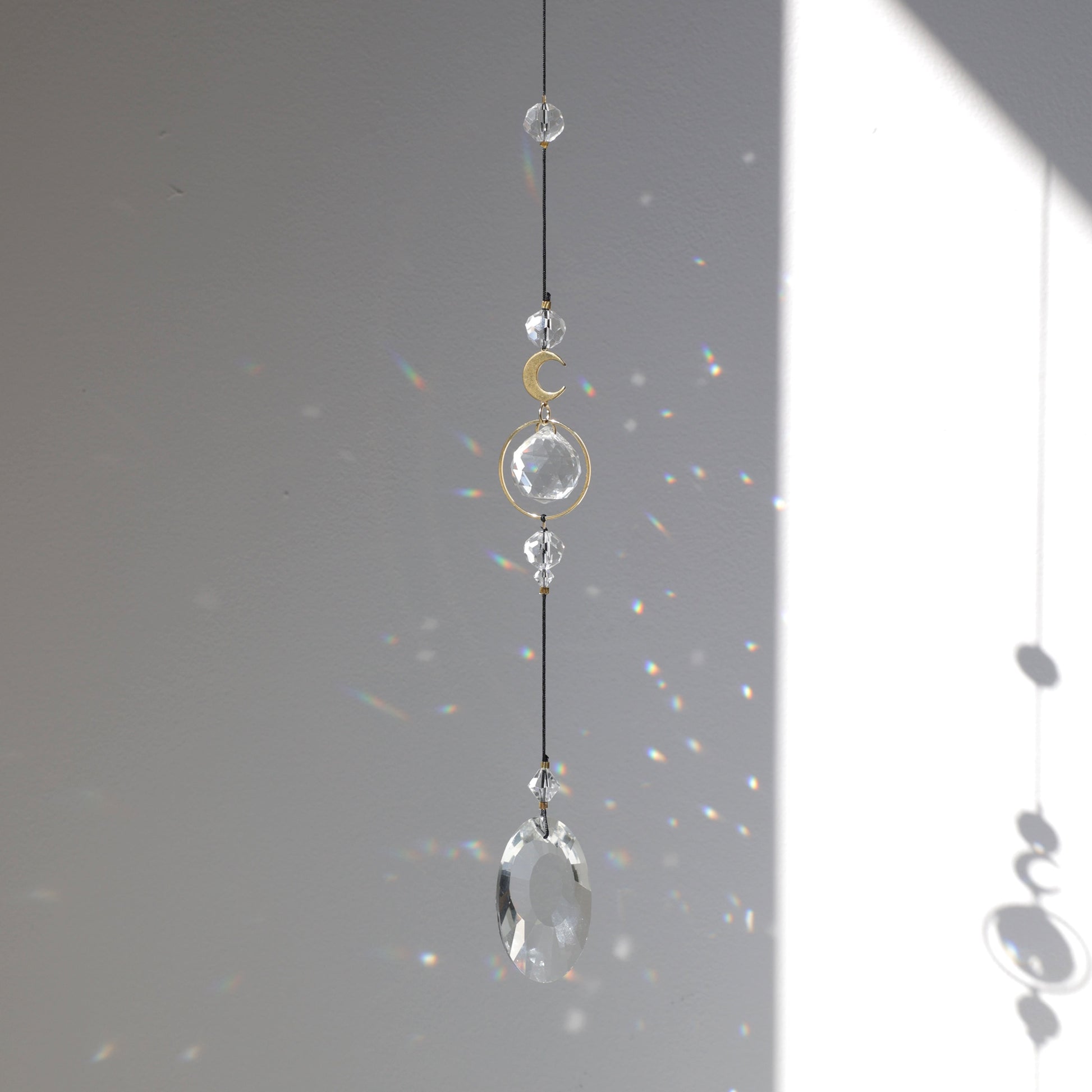 Suncatcher Black Aura de la marque Rayonne suspendu à une fenêtre, capteur de lumière créant des arcs-en-ciel dans la maison.