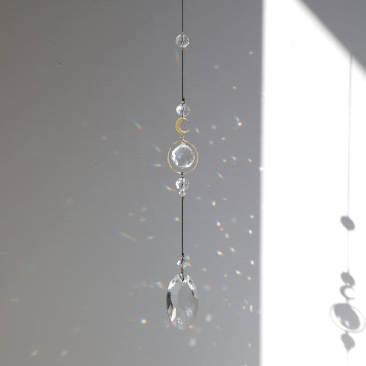 Suncatcher Black Aura de la marque Rayonne suspendu à une fenêtre, capteur de lumière créant des arcs-en-ciel dans la maison.