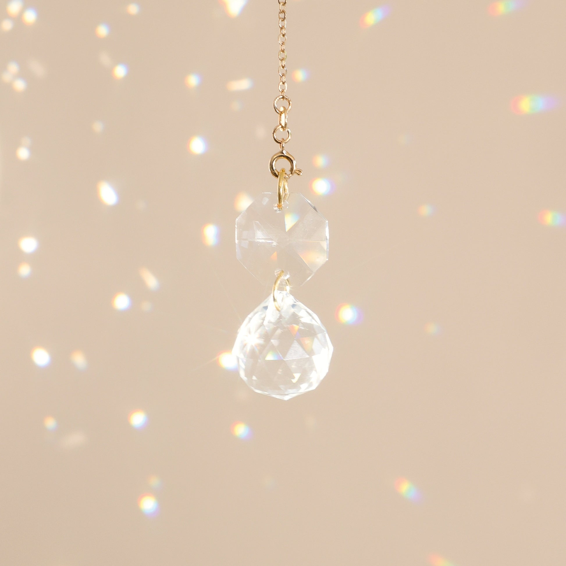 Mini Suncatcher CARAT suspendu près d’une fenêtre, diffusant des reflets arc-en-ciel et créant une ambiance harmonieuse et apaisante.