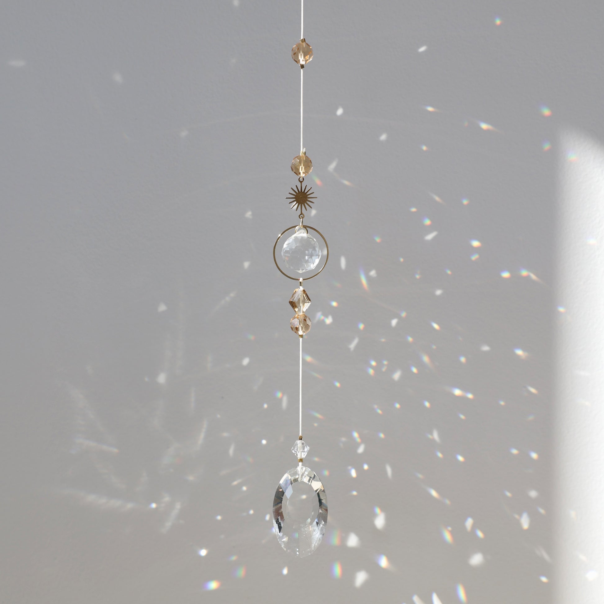 Suncatcher Golden Aura suspendu près d’une fenêtre, diffusant des reflets arc-en-ciel grâce à ses cristaux.
