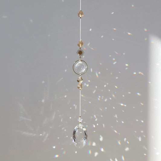 Suncatcher Golden Aura suspendu près d’une fenêtre, diffusant des reflets arc-en-ciel grâce à ses cristaux.