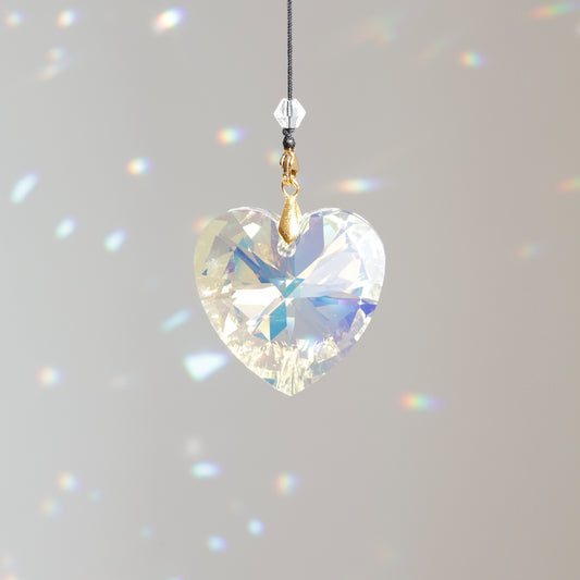 Suncatcher INFINITY clipé à une rallonge, placé au soleil, diffusant des reflets colorés et apportant énergie positive à la pièce.