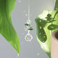 Petit Suncatcher en cristal transparent et vert, accroché à une plante et créant des reflets arcs-en-ciel dans la pièce