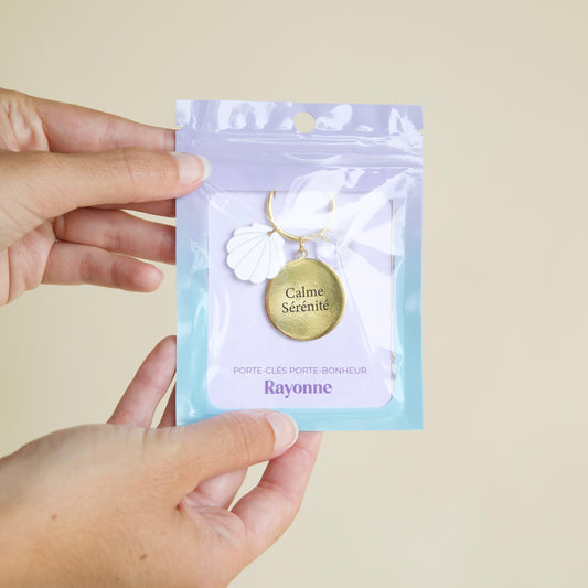 Porte-clés SÉRÉNITÉ avec médaillon gravé, orné d’un charm coquillage en acrylique et d’un cristal transparent, pour inviter calme et sérénité au quotidien.