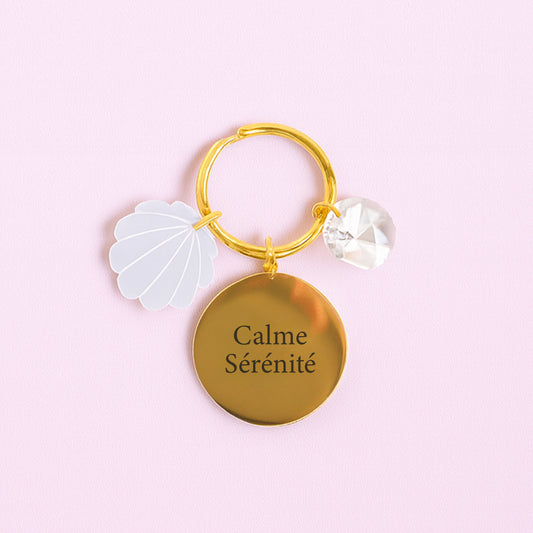 Porte-clés SÉRÉNITÉ Rayonne® avec médaillon gravé, charm coquillage en acrylique et cristal transparent, symbole de paix et sérénité