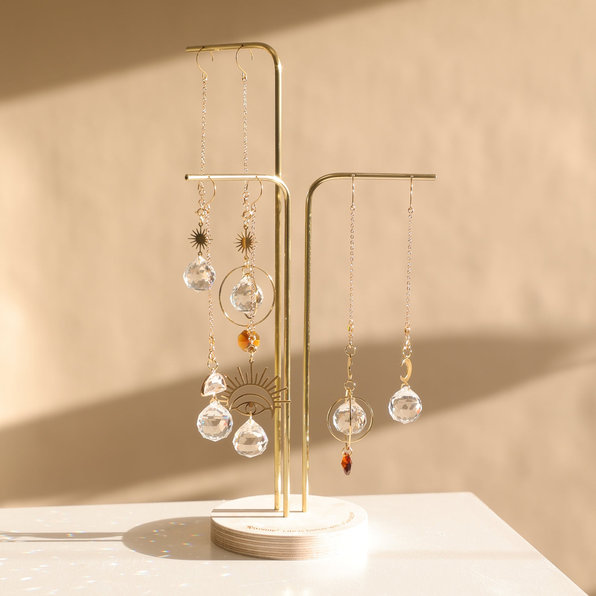 Présentoir Suncatcher en bois et laiton avec 3 tiges, suspendant 6 Suncatchers, sur un comptoir de boutique.