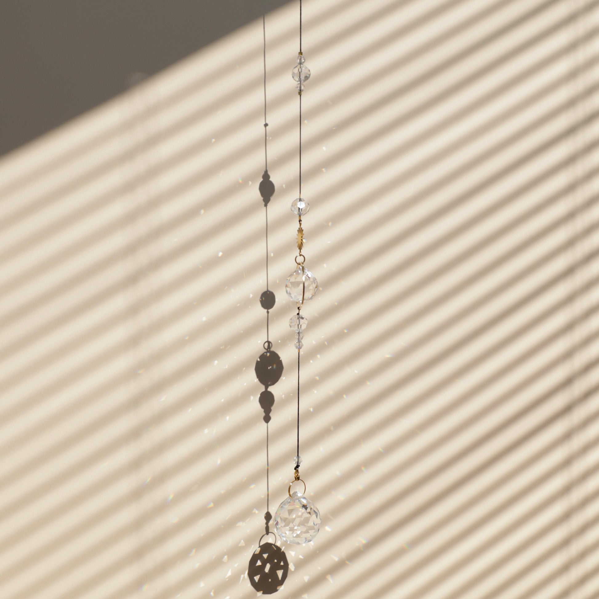 Rallonge HOPE de la marque Rayonne® clipée à un Suncatcher, suspendue près d’une fenêtre ensoleillée, projetant de magnifiques reflets arc-en-ciel dans la pièce.