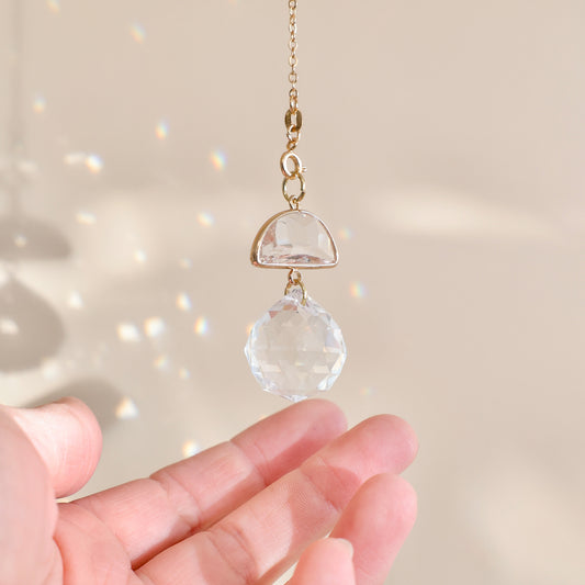 Suncatcher SKY SNOW suspendu près d’une fenêtre, diffusant des reflets arc-en-ciel et apportant une ambiance apaisante.