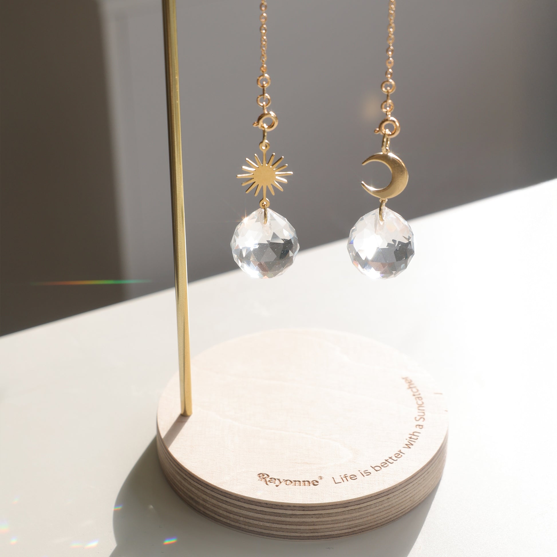 Détail des Suncatchers Rayonne installés sur le présentoir, captant la lumière et créant des reflets arc-en-ciel.