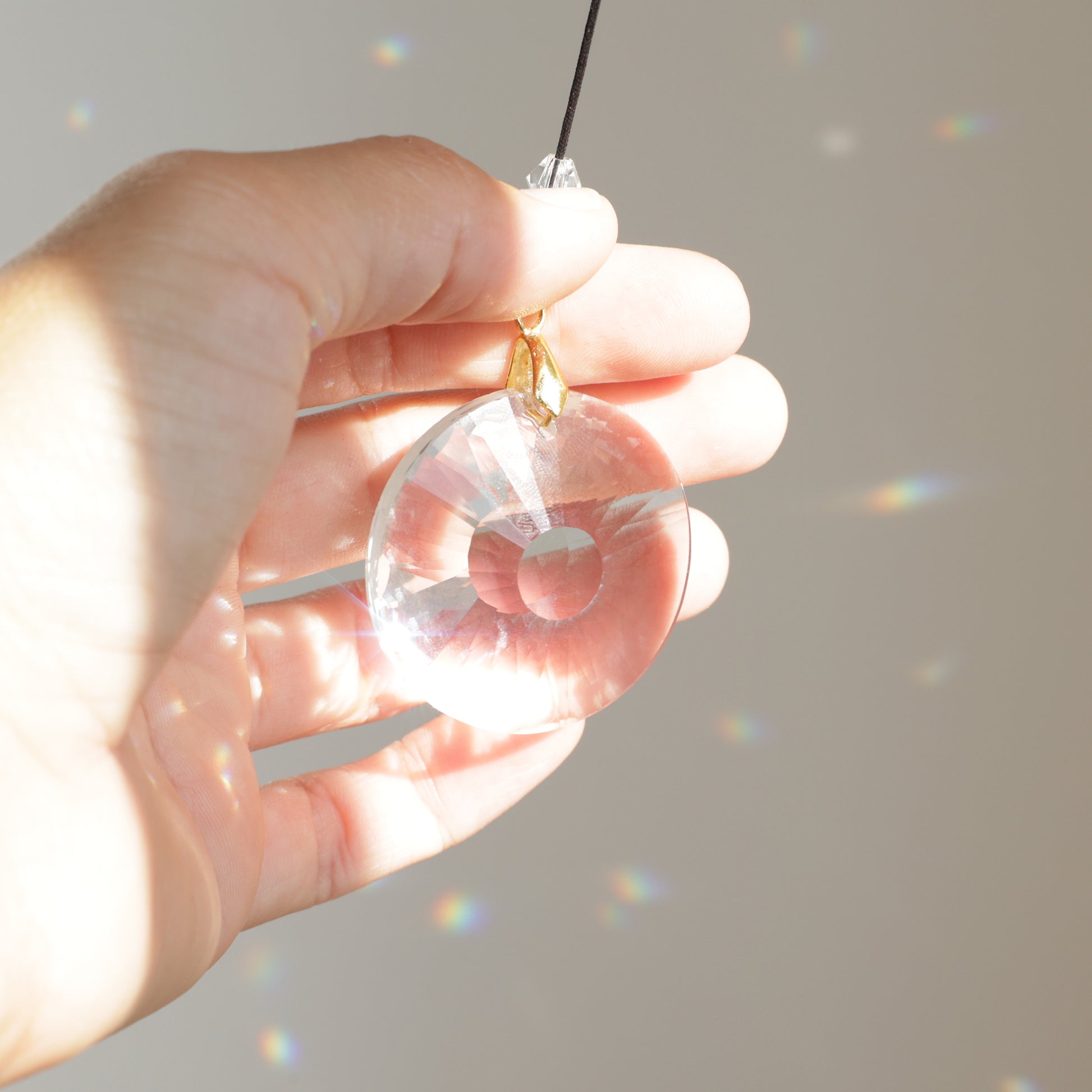 Sucnatcher CIRCLE Rayonne® clipé à une rallonge, suspendu près d’une fenêtre ensoleillée et créant une ambiance douce et apaisante avec ses reflets arc-en-ciel.