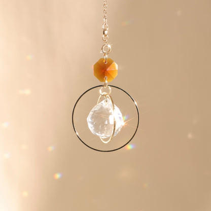 Suncatcher EVERLIGHT ambre exposé au soleil, diffusant des reflets lumineux pour renforcer la stabilité et l’équilibre intérieur.
