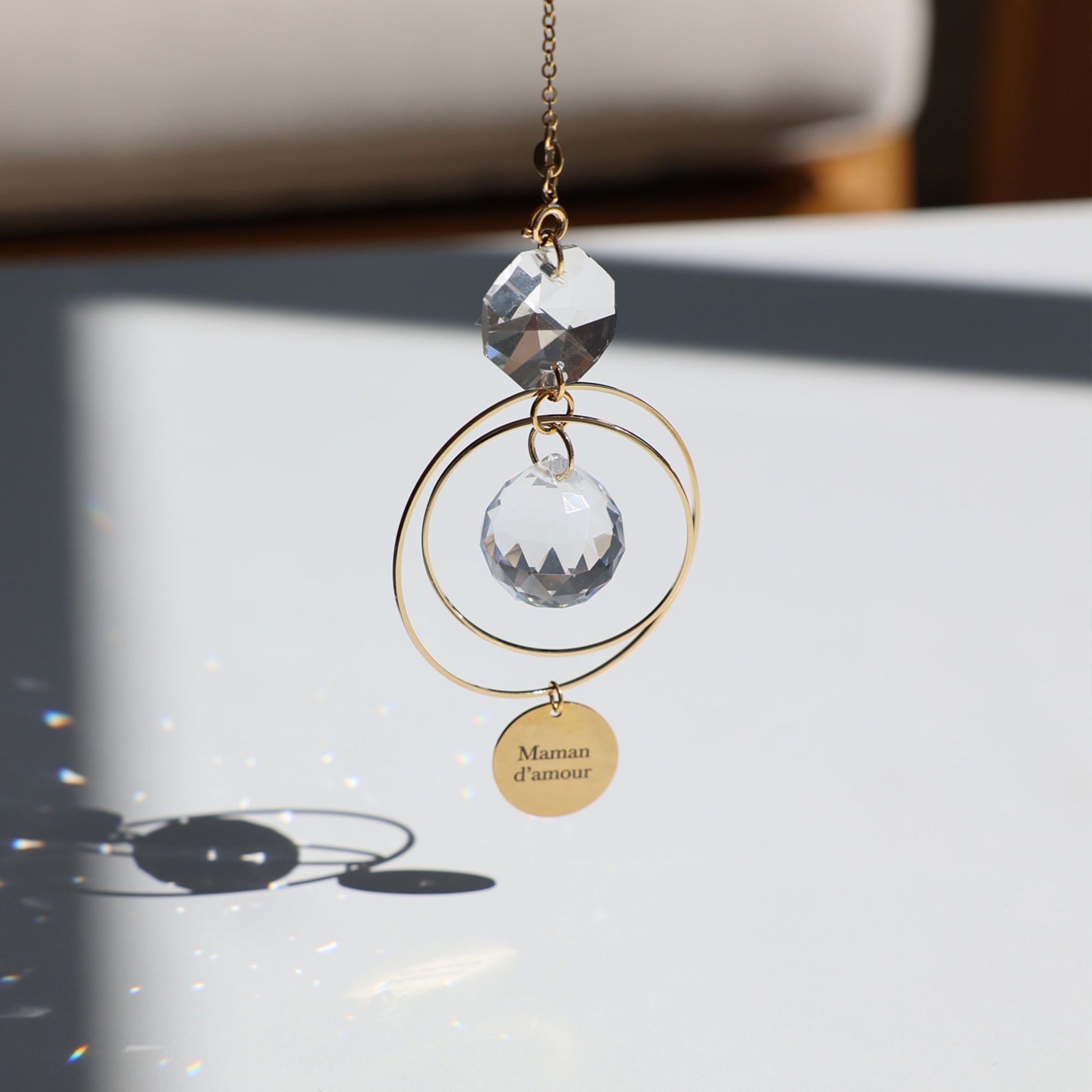 Suncatcher MAMAN en verre, suspendu près d'une fenêtre, prêt à capter les rayons du soleil.