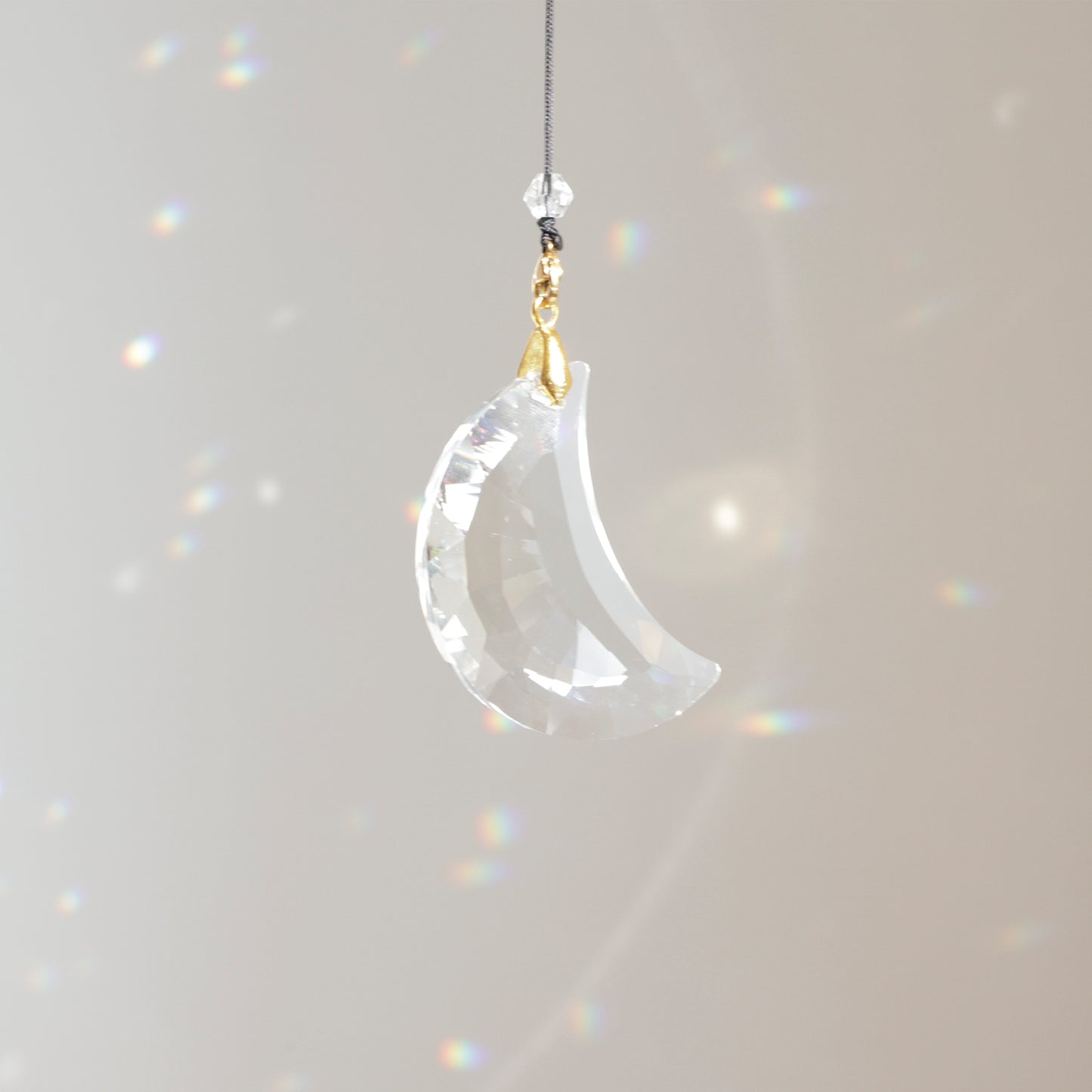 Suncatcher MOONLIGHT clipé à une rallonge, placé près d’une fenêtre ensoleillée et créant un jeu de reflets colorés dans la pièce.