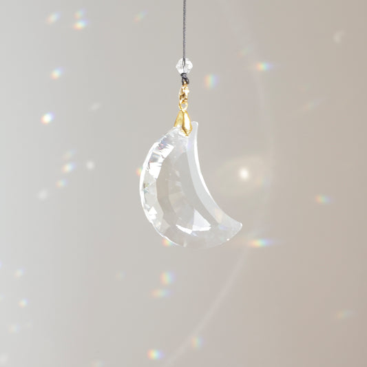 Suncatcher MOONLIGHT clipé à une rallonge, placé près d’une fenêtre ensoleillée et créant un jeu de reflets colorés dans la pièce.