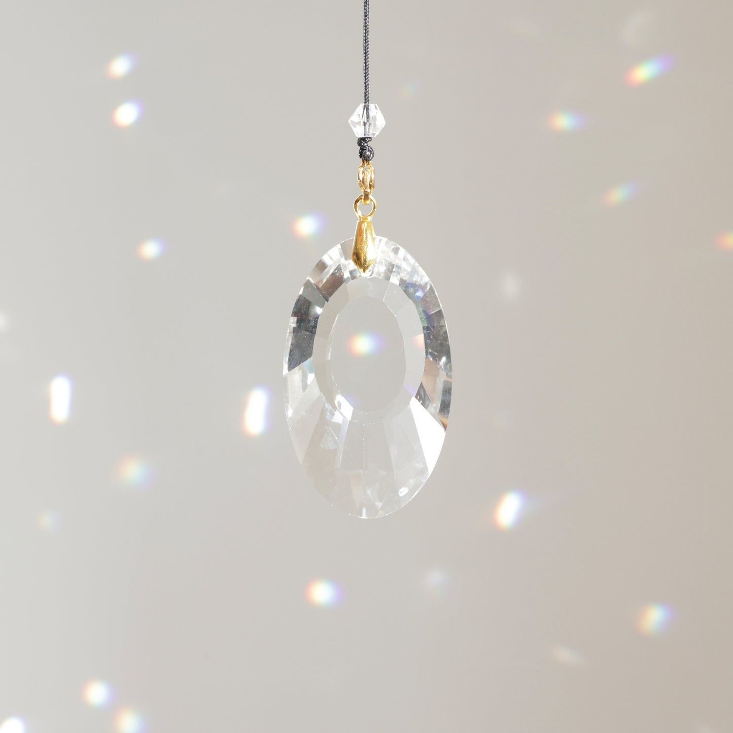 Cristal OPALE clipé à une rallonge, suspendu au soleil, projetant des reflets lumineux et colorés dans la pièce.