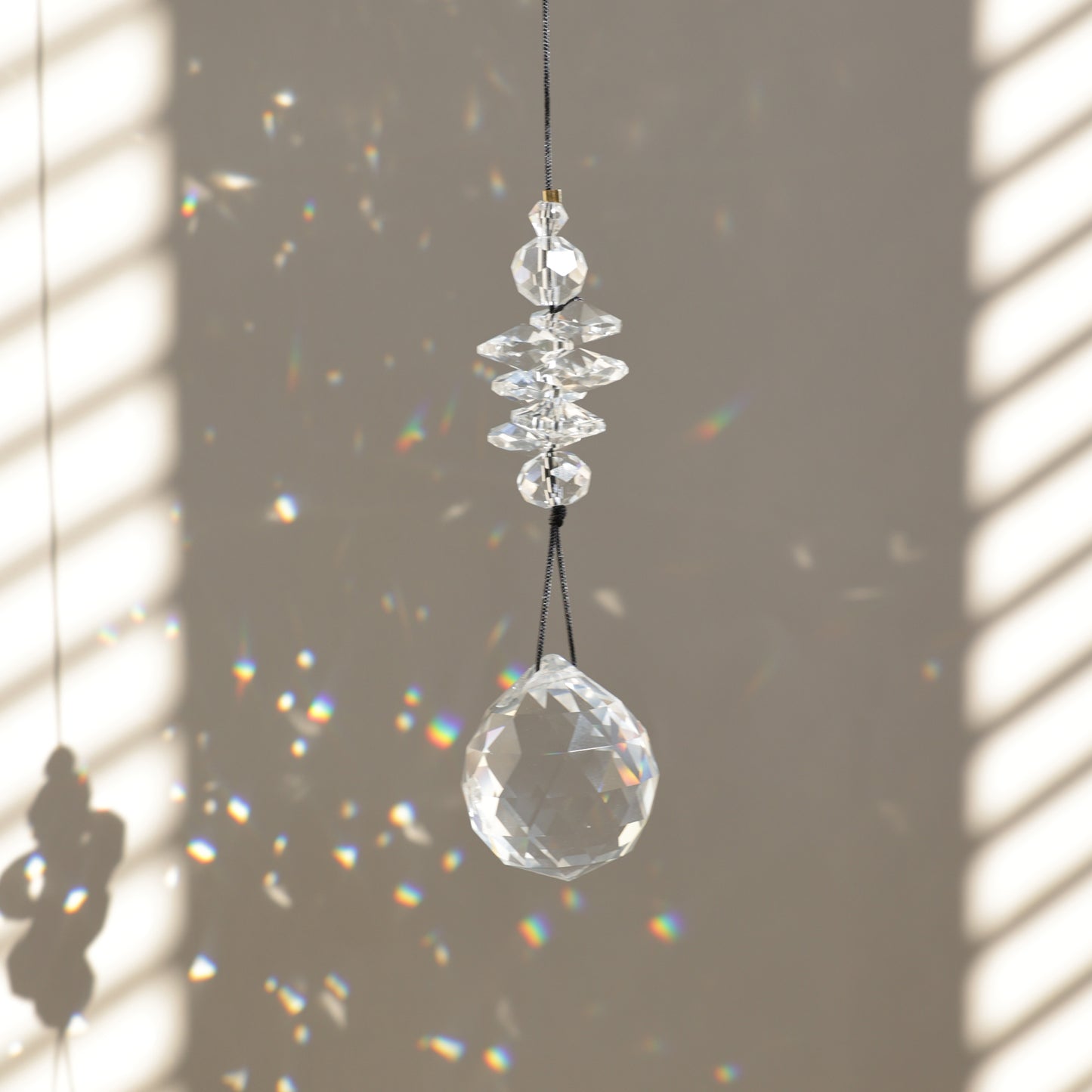Suncatcher PEARL de Rayonne® suspendu, diffusant des reflets arc-en-ciel grâce à ses cristaux transparents.