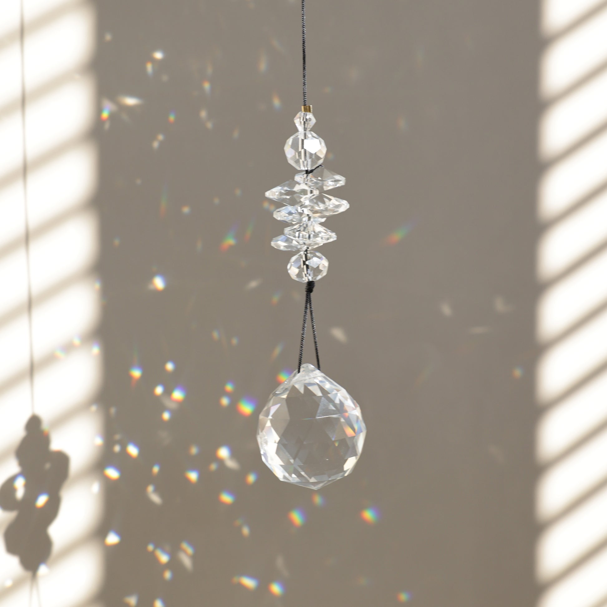 Suncatcher PEARL de Rayonne® suspendu, diffusant des reflets arc-en-ciel grâce à ses cristaux transparents.
