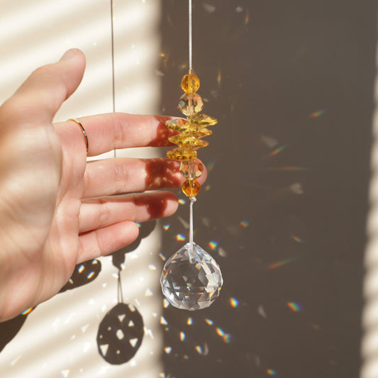 Suncatcher Solstice transparent et jaune suspendu, diffusant des reflets arc-en-ciel à travers ses cristaux