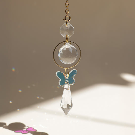Suncatcher papillon REFLET Rayonne® accroché à une fenêtre, diffusant des reflets arc-en-ciel et symbolisant le renouveau.
