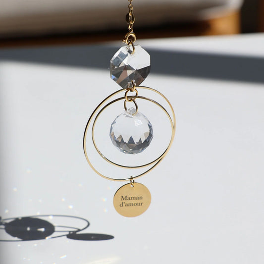 Suncatcher MAMAN en verre, suspendu près d'une fenêtre, prêt à capter les rayons du soleil.