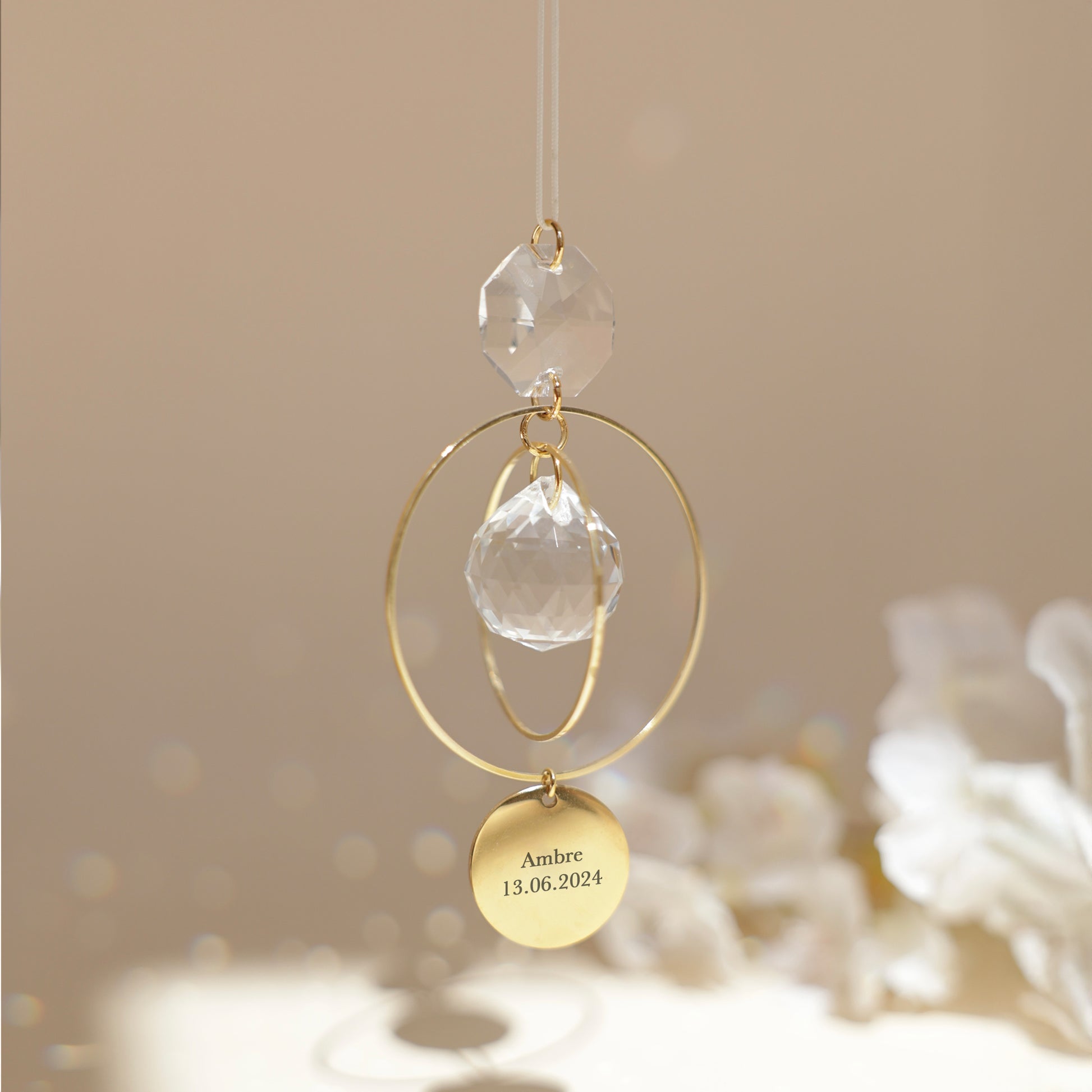 Suncatcher Jeanne personnalisé suspendu près d'une fenêtre, projetant de magnifiques reflets arc-en-ciel grâce à son cristal. Capteur de lumière artisanal en laiton doré, idéal pour une décoration bohème et apaisante. Cadeau unique et gravé, fabriqué à la main en France
